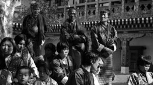 A seated group of people in fine clothes watch a historical reenactment. 