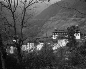 Traditional Dzong, a combination of a fort and monastery, representing the secular body and military force. The Dzong is settled amongst a verdant mountainous terrain. 
