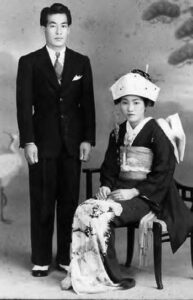 photo of a man and woman next to each other. the man wears a suit and the woman sits in kimono.