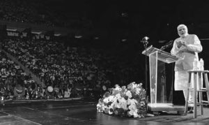 photo of an old man speaking in front of a large crowd