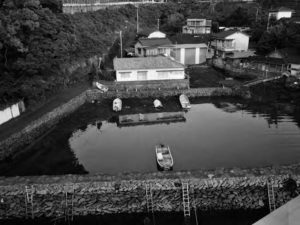 A building sits on the water, across from a fishing boat sitting in reeds. A boat is parked in the water. 