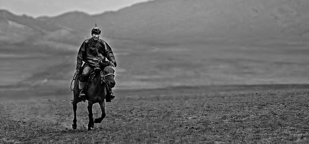 Mongolian horseman in traditional costume rides into the desert. 