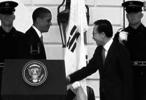 photo of two men in suits shaking each other's hands, flanked by two men in military uniforms