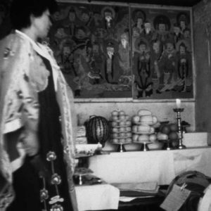 photo of a woman walking by tables full of offerings and a mural