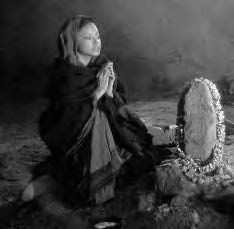 a woman sits with her hands clasped in prayer by a rock