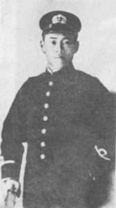 Photograph of young adult Yamamoto pensively staring into the camera. He is wearing a military hat and outfit. 