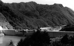 Photograph of a large hydrodam located amongst a mountainous landscape. This illustrates how hydrodams have significantly altered Japan's landscape. 