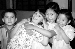 four young children, three girls and a boy, hold each other and smile