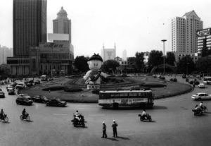A round about city road with skyscrapers in the background and traffic on the road. 