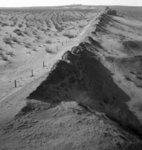 the landscape is sandy. Poking out of the sand like spines are broken remnants of a wall