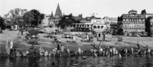 Photo of some buildings along the Ganges River and some people standing on the river