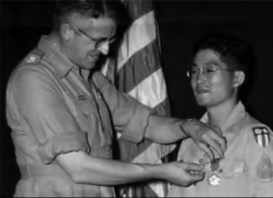 A US soldier places a metal on a Japanese soldier. 