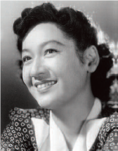 A photograph of a young Setsuko Hara, a young adult Asian woman. She is wearing a polka dot dress and has a radiant smile on her face, exuding beauty and joy.