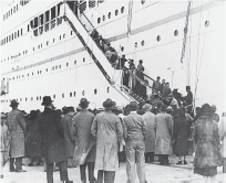 Jewish refugees disembark a large ship into a crowd of people. 