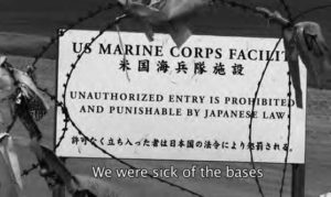 photo of a sign wrapped in barbed wire, stating "US Marine Corps Facility. unauthorized entry is prohibited and punishable by Japanese law". the screencap says "we were sick of the bases"