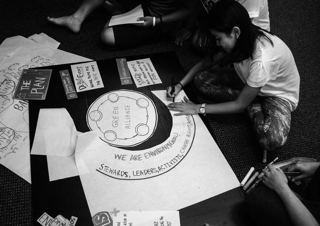 Students sit at a table working on poster cutouts and signs. 