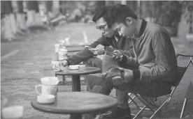 two men sit at a cafe table with coffee cups in front of them