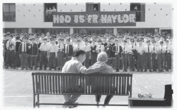 two people sit on a bench while a crowd of people look on