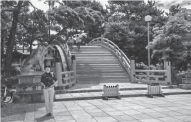 A person standing in front of the Komainu guardian lion-dog statue at the Nishiotorii gate to the Sumiyoshi Shrine. The statue stands tall and imposing, representing a traditional Japanese cultural and religious symbol.