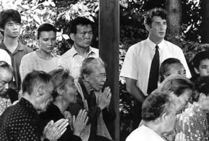 an image of several older people with their hands clasped in prayer, while some younger people look on.