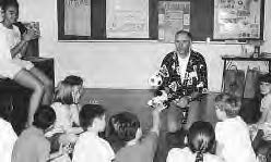 several students sit in front of a man with a ball and stuffed animal