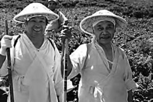 two men in white robes and straw hats smile at the camera