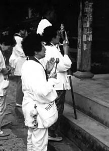 people in white robes stand with their hands up, palms facing towards the sky.