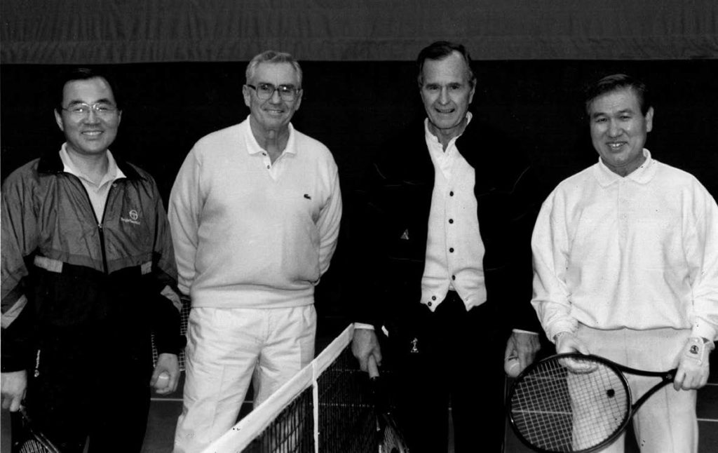 Group of four smiling men holding tennis rackets.