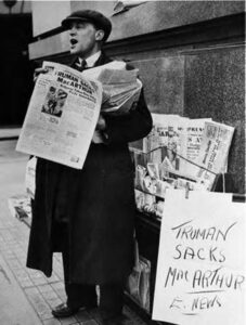 a man holds newspapers and yells