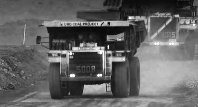 Mining trucks travel down a dirt road. 