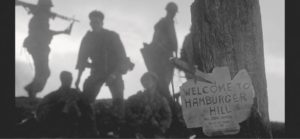 photo of men walking to a sign saying welcome to hamburger hill