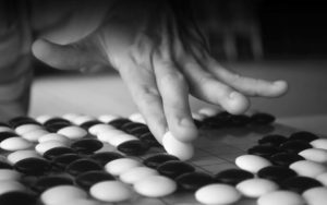 Close-up of a Go player’s hand showing how to hold and place a stone on the crowded board